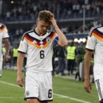 Drie Duitse spelers in witte wedstrijdtenues lopen teleurgesteld over het veld na een wedstrijd.