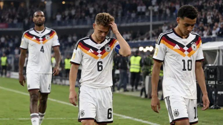 Drie Duitse spelers in witte wedstrijdtenues lopen teleurgesteld over het veld na een wedstrijd.