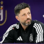 Een medewerker van Anderlecht tijdens een persmoment voor een paarse clubachtergrond.