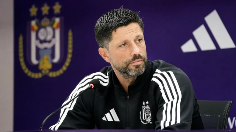 Een medewerker van Anderlecht tijdens een persmoment voor een paarse clubachtergrond.