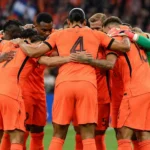 Nederlandse spelers in oranje tenue vormen samen met hun doelman een kring op het veld.
