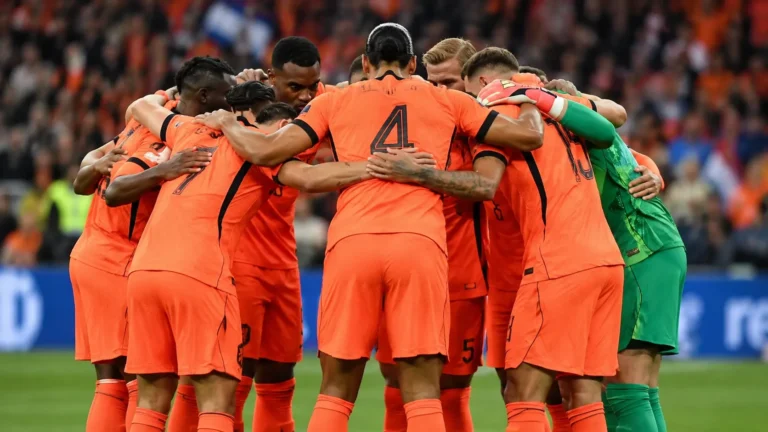 Nederlandse spelers in oranje tenue vormen samen met hun doelman een kring op het veld.
