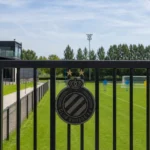 Leeg trainingsveld voor beloften met een vast Club Brugge-embleem aan de toegangspoort.