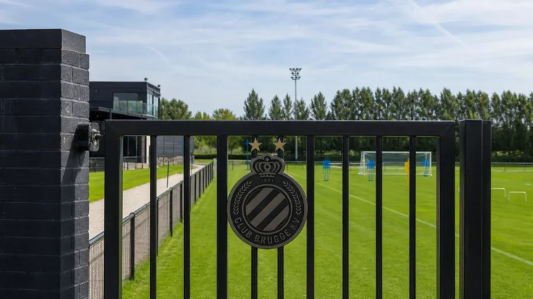 Leeg trainingsveld voor beloften met een vast Club Brugge-embleem aan de toegangspoort.