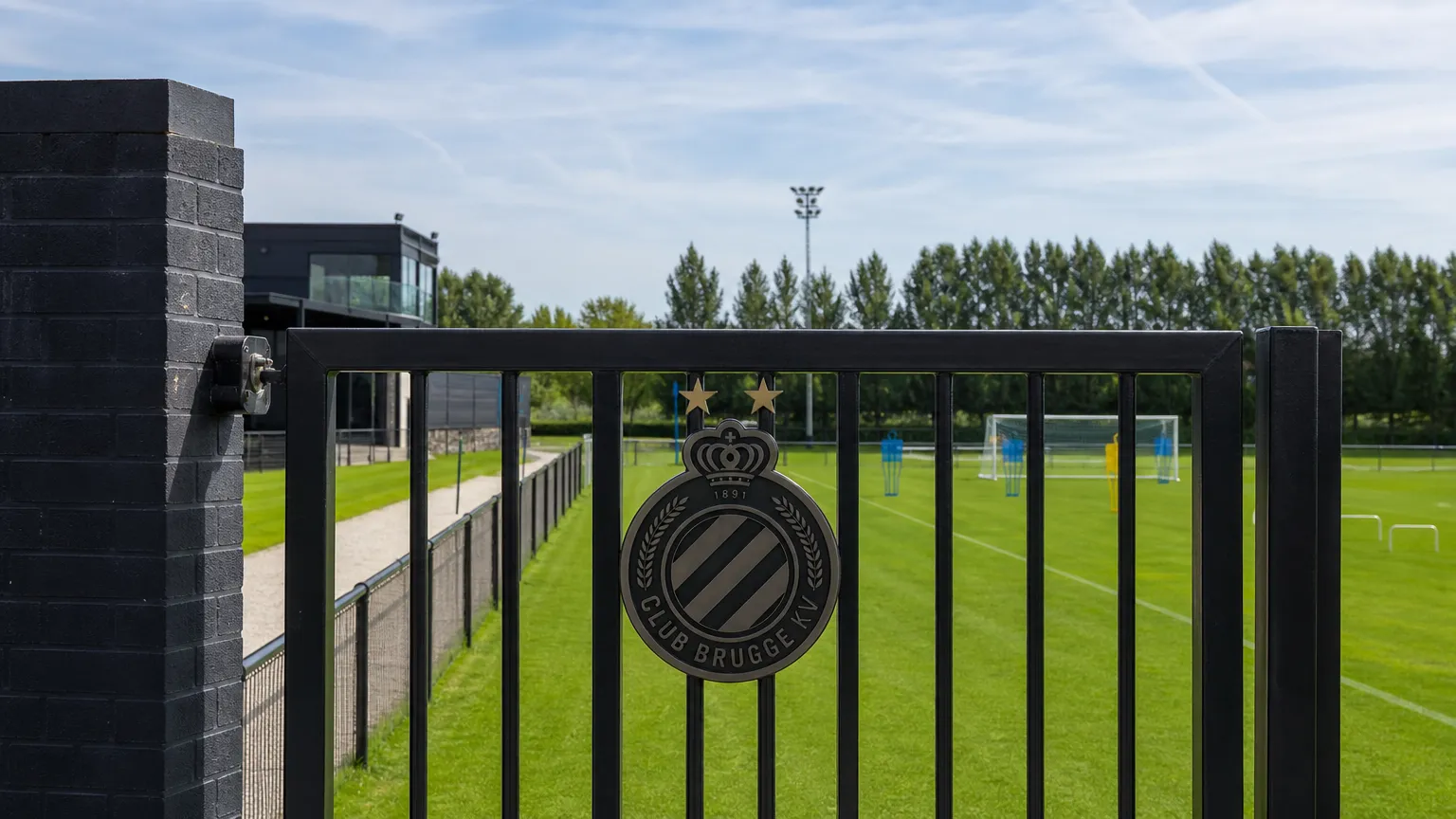 Leeg trainingsveld voor beloften met een vast Club Brugge-embleem aan de toegangspoort.