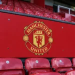 Manchester United-embleem op een rood paneel voor stadionzitjes.