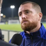 Gill Swerts tijdens een interviewmoment aan een voetbalveld.