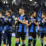 Een groep spelers van Club Brugge applaudisseert op het veld in blauw-zwarte wedstrijdkleding.