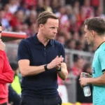 Een lid van de technische staf van Standard staat langs de zijlijn tussen spelers.