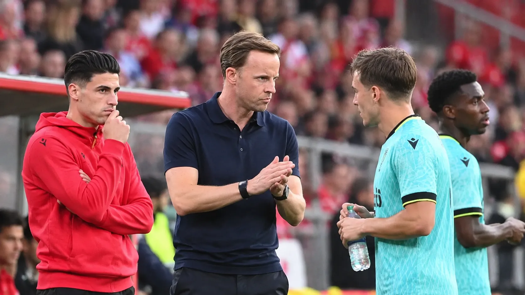 Een lid van de technische staf van Standard staat langs de zijlijn tussen spelers.