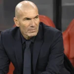 Zinédine Zidane spreekt in een persruimte in een donker pak.