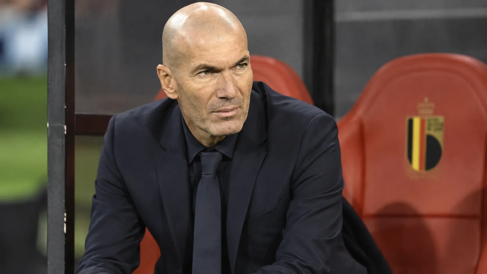 Zinédine Zidane spreekt in een persruimte in een donker pak.