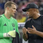 Een doelman van Bayern München in groen overlegt op het veld met een coach in donkere kleding.