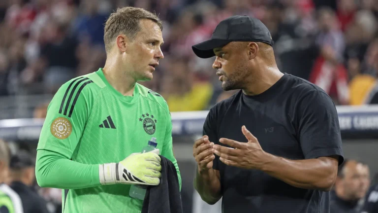 Een doelman van Bayern München in groen overlegt op het veld met een coach in donkere kleding.