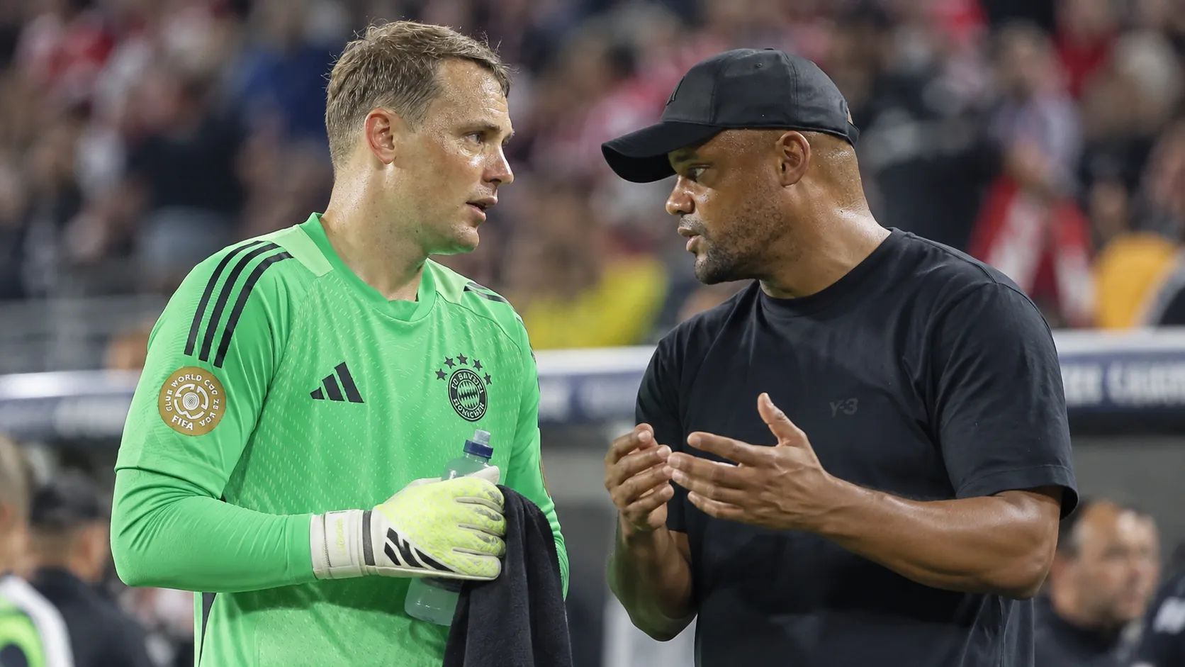 Een doelman van Bayern München in groen overlegt op het veld met een coach in donkere kleding.