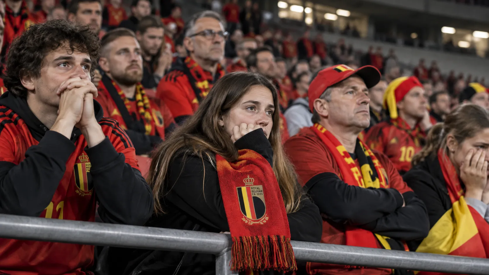 Belgische supporters in rode sjaals reageren teleurgesteld in de tribunes na een interland.