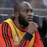 Romelu Lukaku zit in Belgische warming-upkleding op de spelersbank in een stadion.