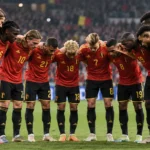 Een groep Belgische internationals in rode tenues tijdens een teamhuddle in een verlicht stadion.