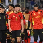 Een groep Belgische spelers in rood loopt langs de zijlijn van een verlicht stadion.