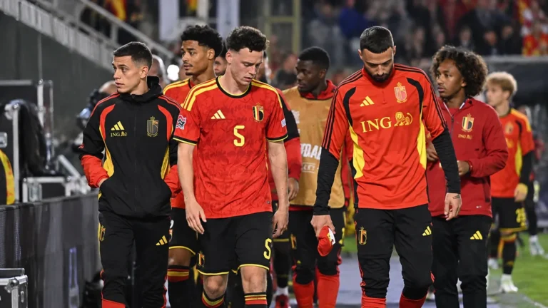 Een groep Belgische spelers in rood loopt langs de zijlijn van een verlicht stadion.