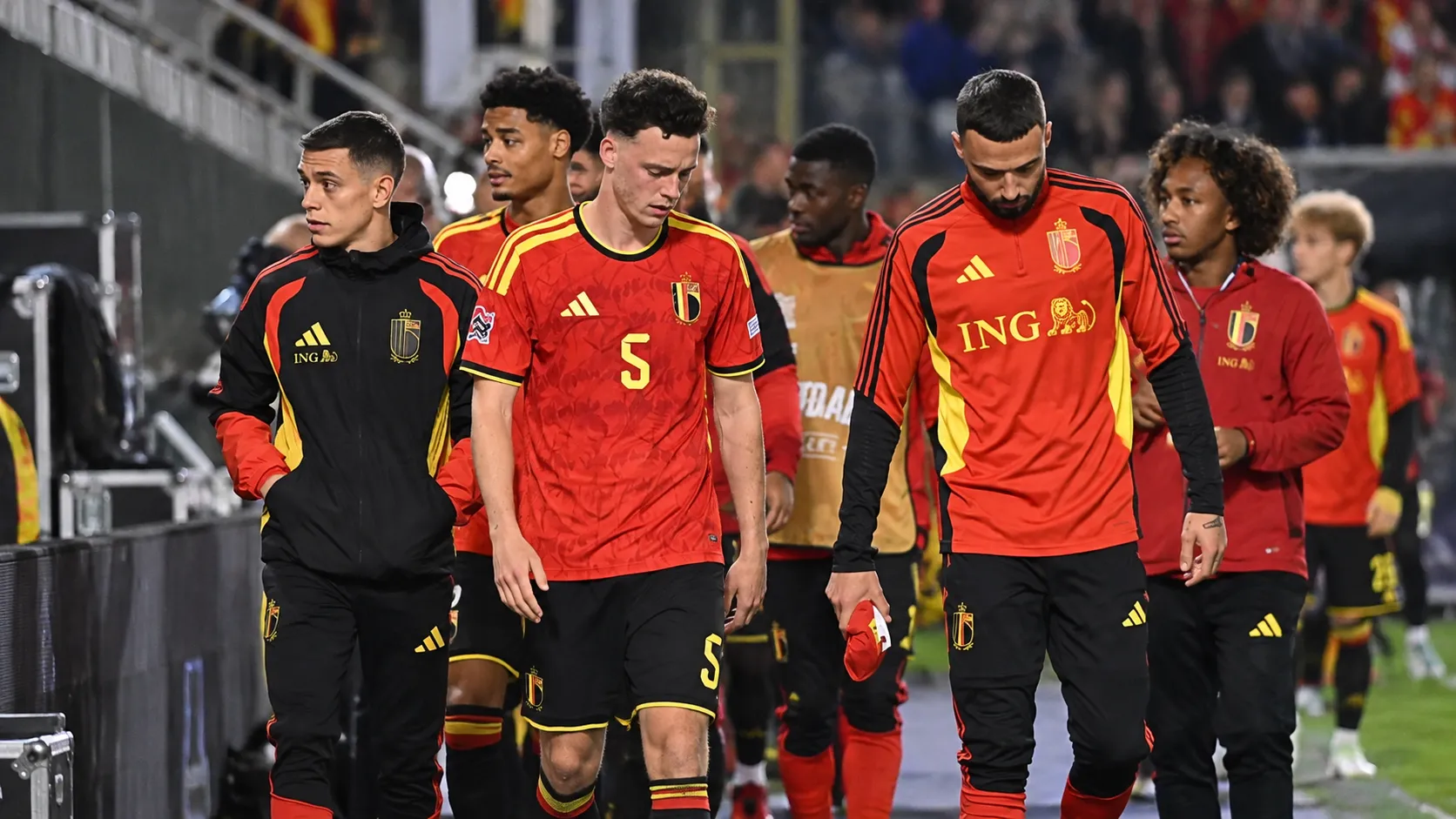 Een groep Belgische spelers in rood loopt langs de zijlijn van een verlicht stadion.
