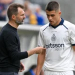 Een Club Brugge-coach spreekt langs het veld met een speler in een wit wedstrijdshirt.