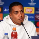 Youri Tielemans in een wit trainingsjack tijdens een mediamoment na de wedstrijd.