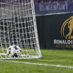 Een bal ligt in het doelnet naast een veldbord van de Ronaldinho's Legends Cup.