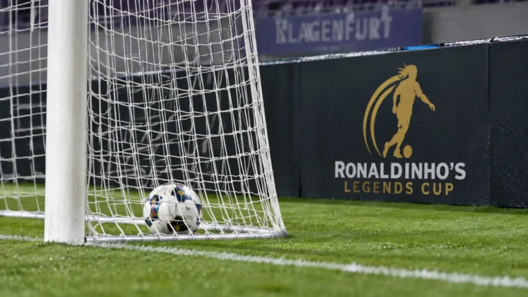 Een bal ligt in het doelnet naast een veldbord van de Ronaldinho's Legends Cup.
