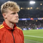 Een Belgische speler in een rood trainingsjack staat na de wedstrijd aan de rand van het veld.