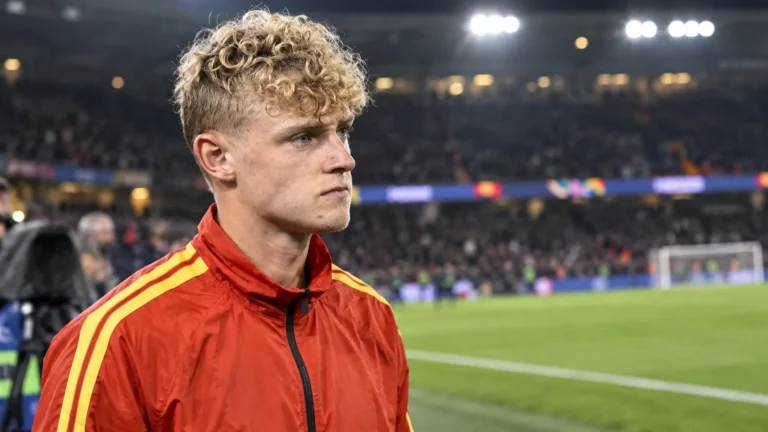 Een Belgische speler in een rood trainingsjack staat na de wedstrijd aan de rand van het veld.