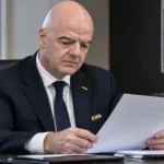 Gianni Infantino schrijft aan een bureau in een formele werkomgeving.