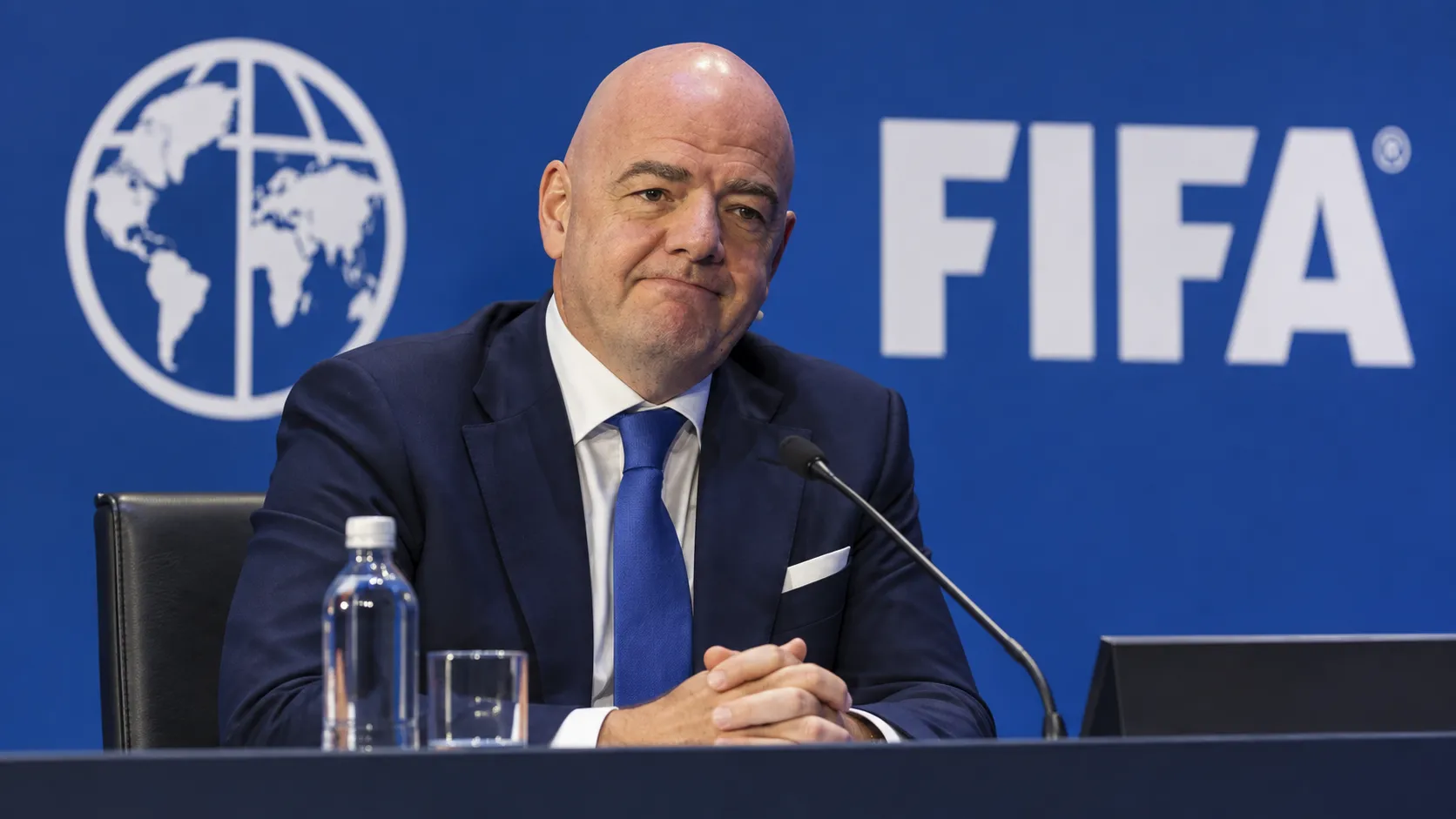 Een niet-spelende official in donker pak tijdens een FIFA-conferentie.