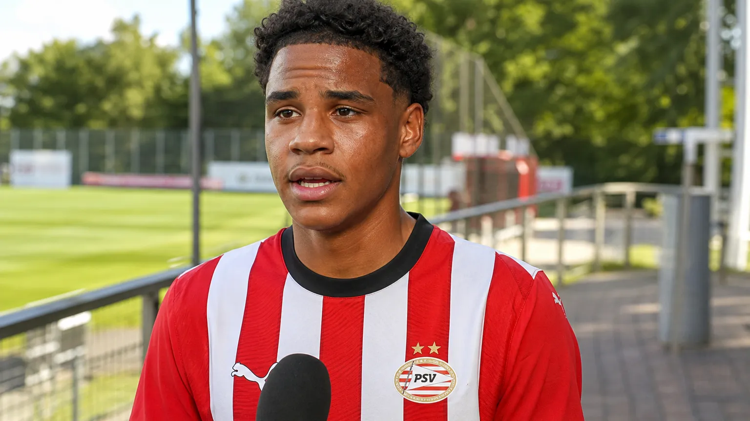 Noah Fernandez in PSV-shirt tijdens een rustig media-interview naast het veld.
