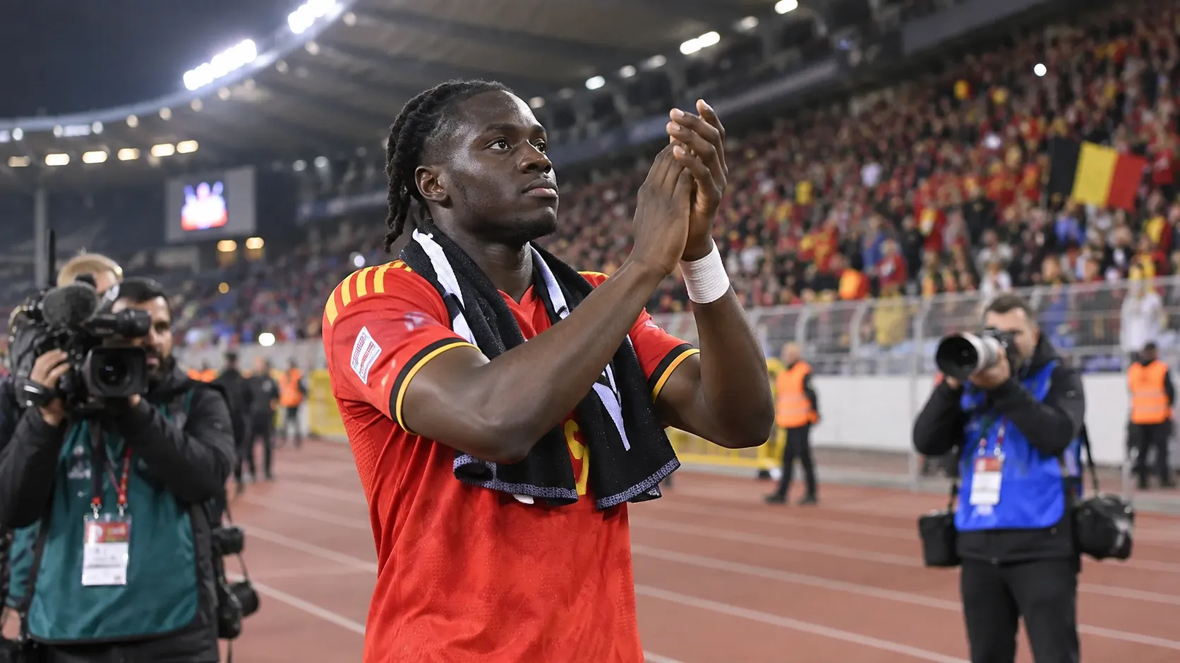 Roméo Lavia applaudisseert in een rood België-tenue langs de atletiekpiste van een stadion.