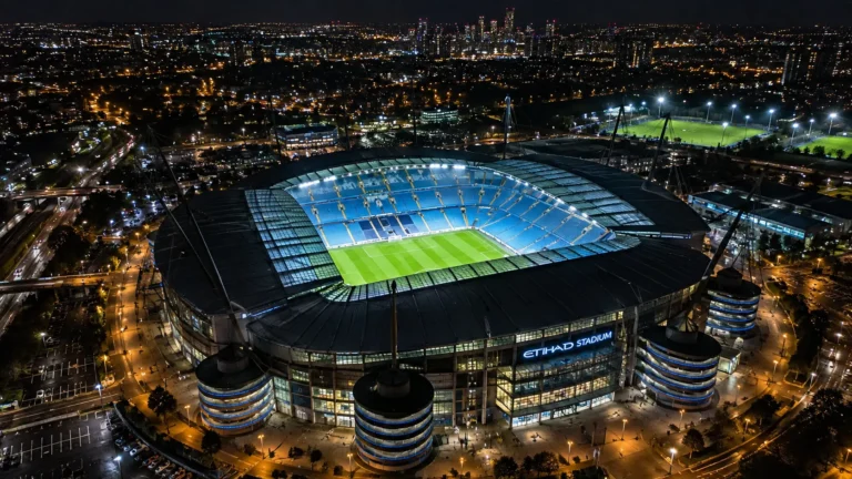 Luchtbeeld van het verlichte Etihad Stadium bij nacht.