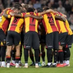 Een groep spelers vormt vlak voor de aftrap een hechte kring op het veld.