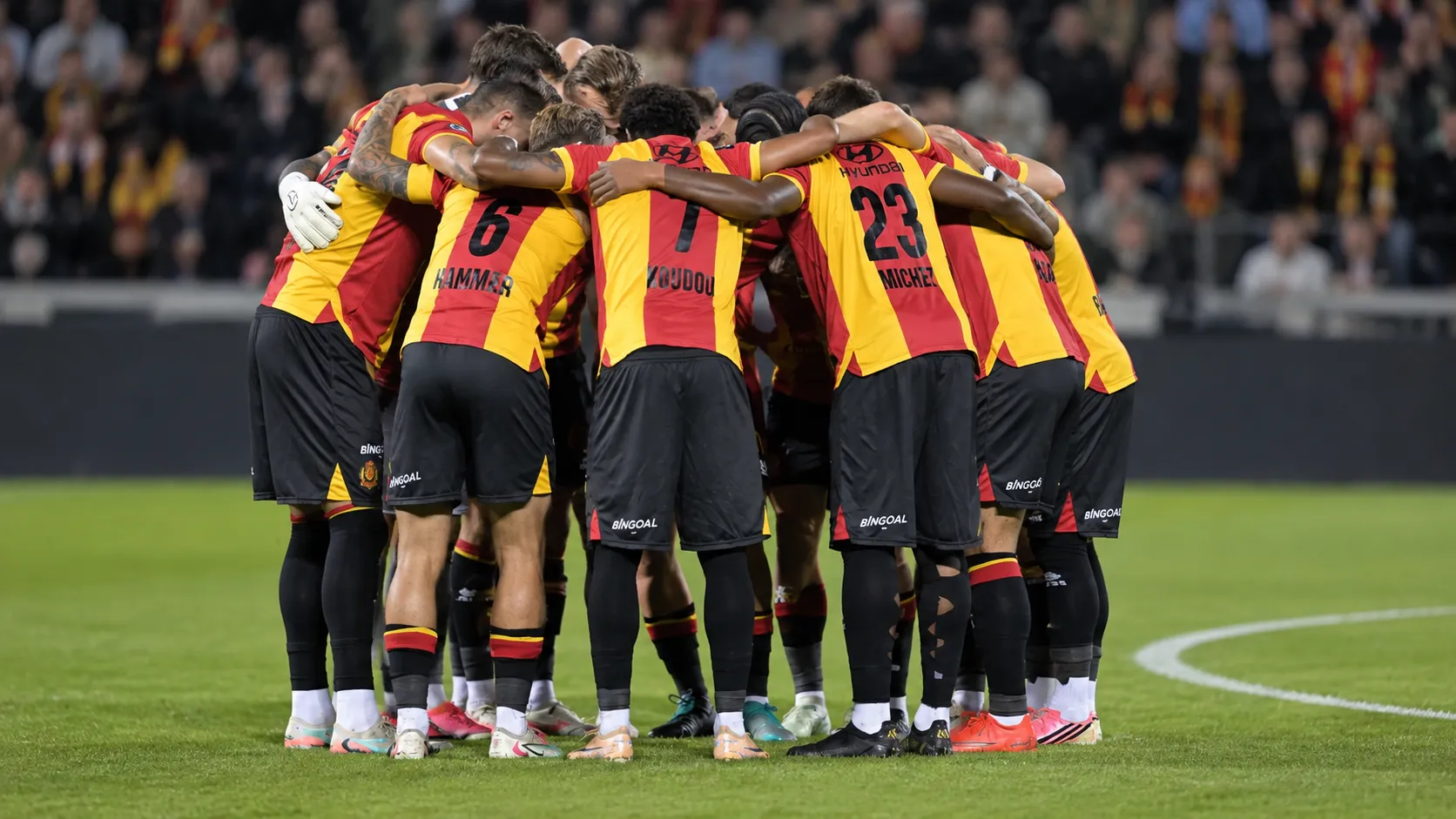 Een groep spelers vormt vlak voor de aftrap een hechte kring op het veld.