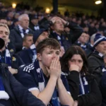 Een collectieve groep Schotse supporters met blauwe sjaals in de tribunes van Hampden Park.