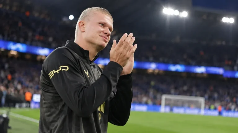 Erling Haaland applaudisseert aan de rand van het veld in donkere Manchester City-kleding.