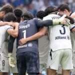 Een groep spelers in lichte tenues vormt een hechte kring op het voetbalveld.