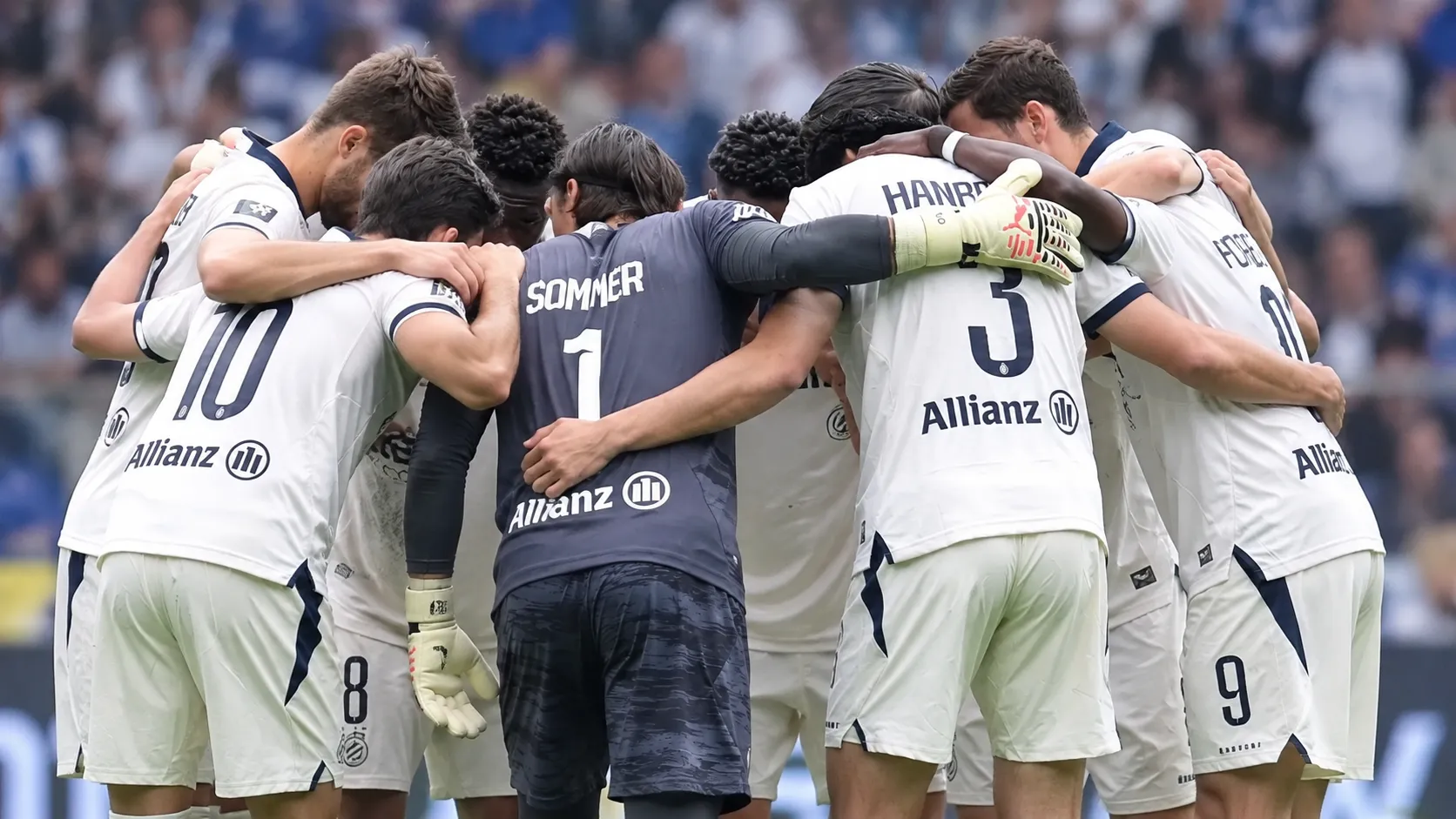 Een groep spelers in lichte tenues vormt een hechte kring op het voetbalveld.