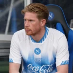 Kevin De Bruyne zit aandachtig op de bank langs het veld in zijn Napoli-wedstrijdshirt.