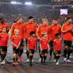 Een groep spelers in rode trainingsjassen wandelt samen op het veld na een interland.