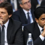 Twee voetbalbestuurders in donkere pakken zitten tijdens een formele bijeenkomst.
