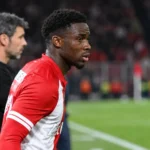 Mandela Keita in een rood-wit wedstrijdshirt langs de zijlijn van een voetbalveld.
