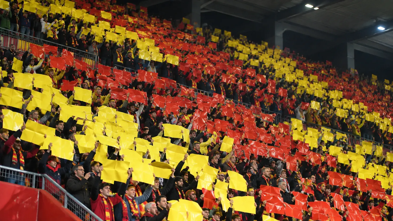 Een volle tribune met supporters die gele en rode kaarten omhooghouden.