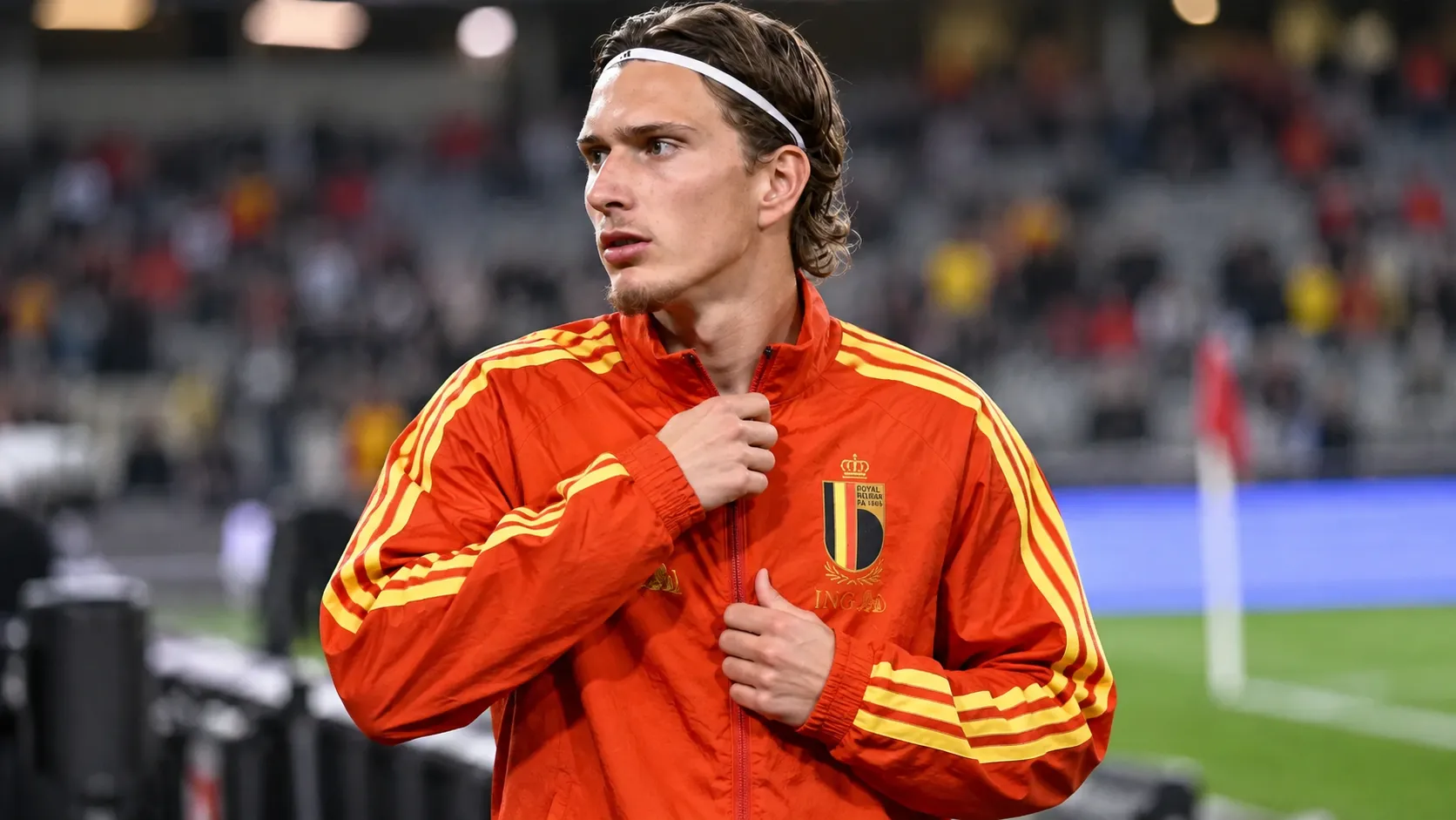 Mika Godts in een trainingsjas van de Rode Duivels tijdens de opwarming in een stadion.