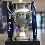 De Croky Cup-trofee met donkerblauwe linten op een sokkel in een indoor voetbalomgeving.