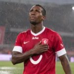 Douglas Teixeira in het rode tenue van FC Twente op een regenachtig voetbalveld.